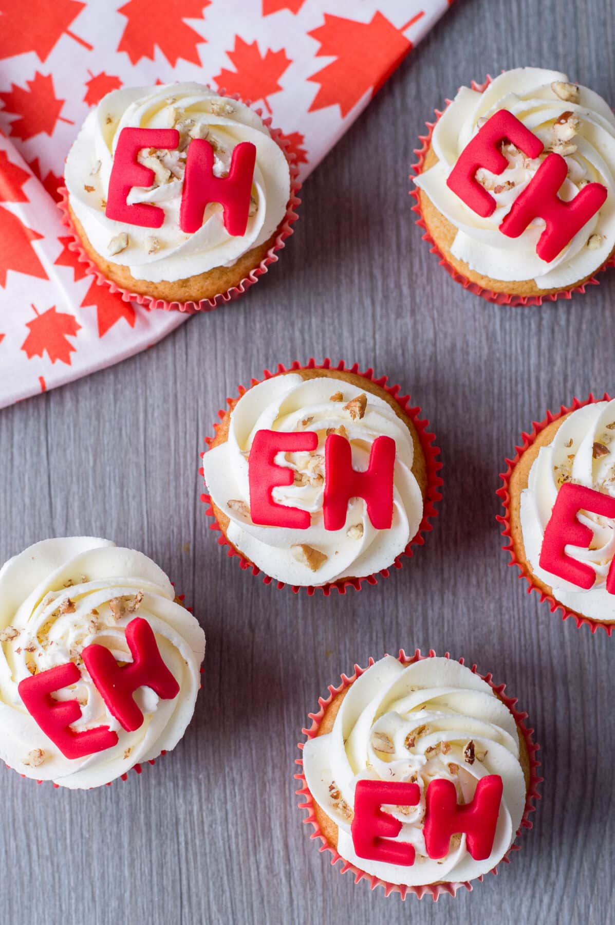Soft maple cupcakes topped with maple buttercream, and fun "Eh" decorations. A festive dessert that's perfect for Canada Day celebrations.