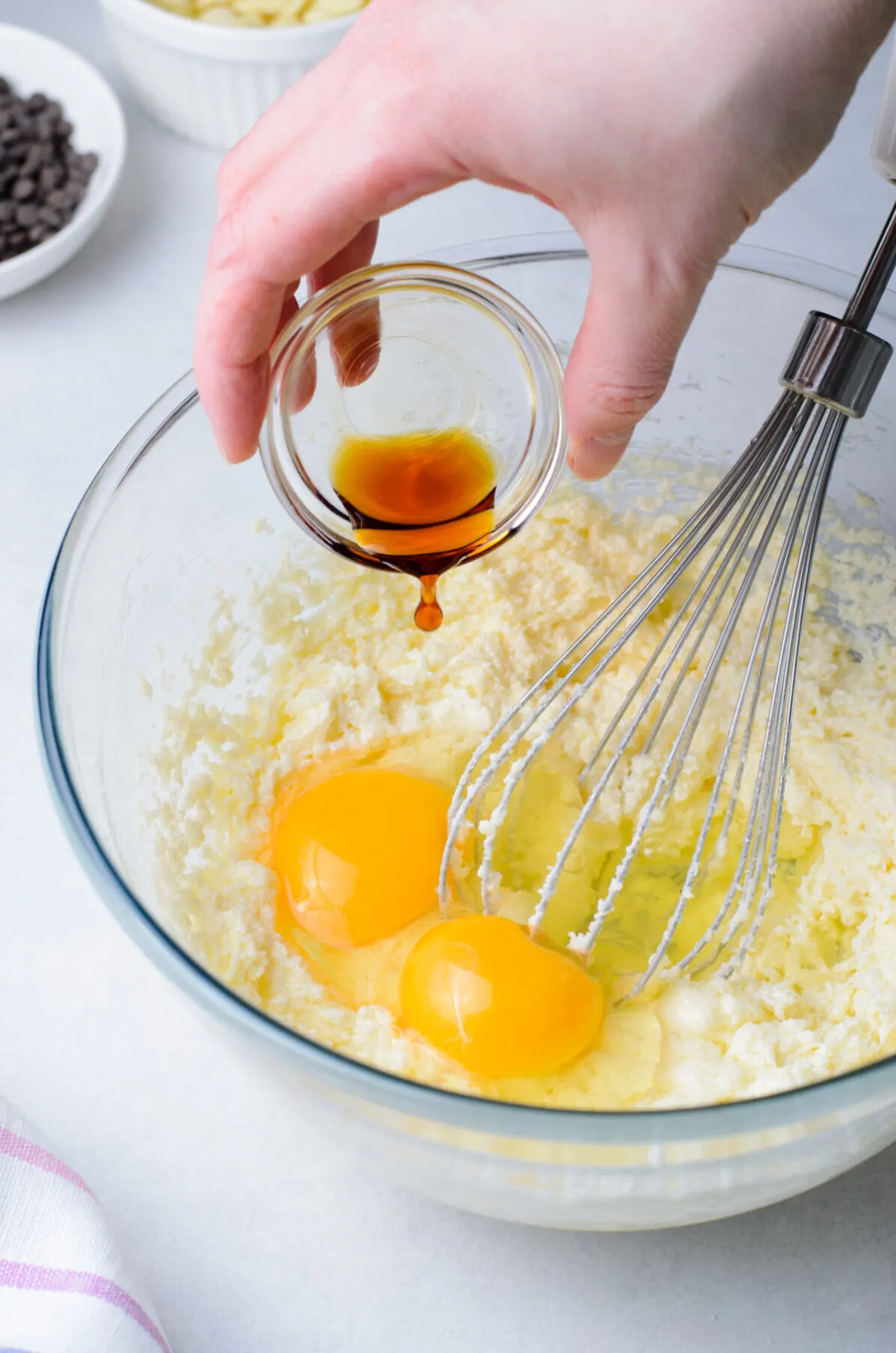 Butter and sugar creamed with two eggs, and vanilla being poured into a bowl.