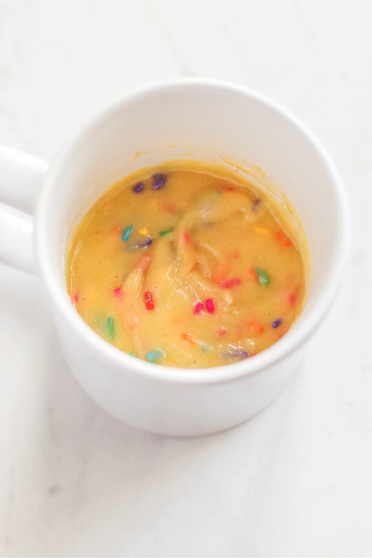 Sprinkles mixed into the batter in the mug.