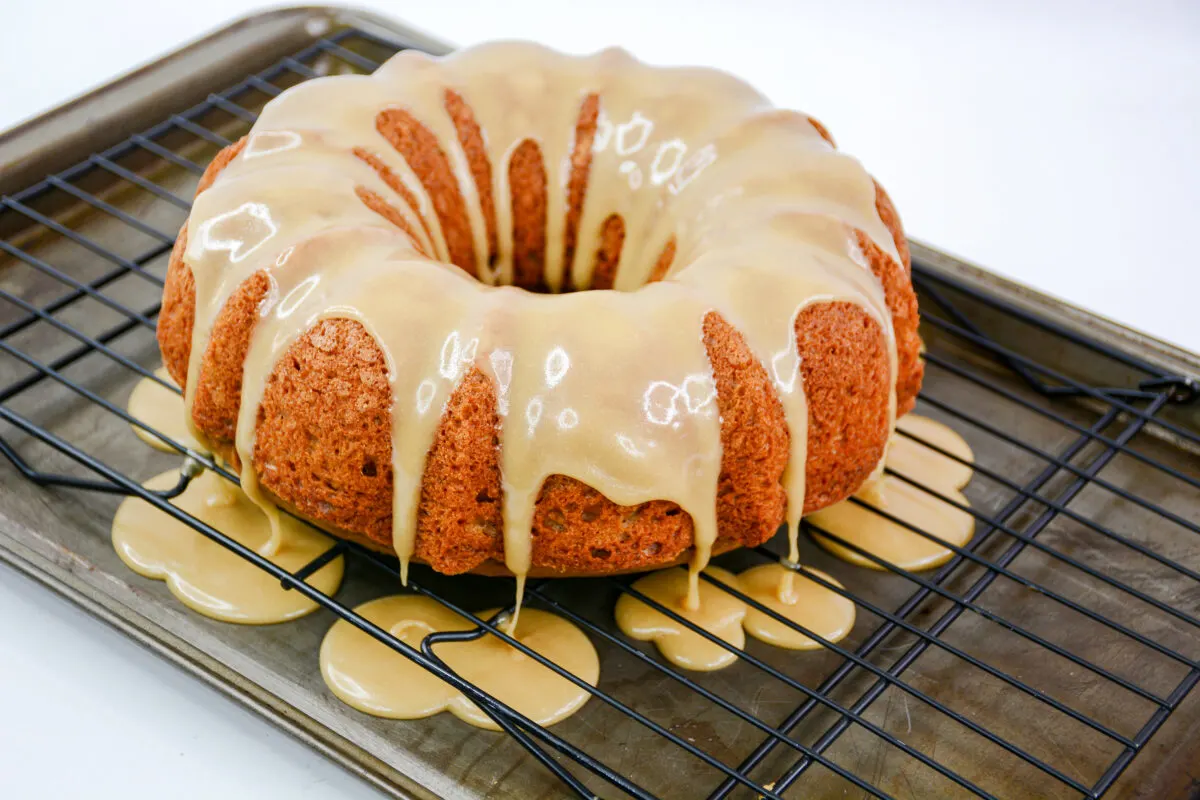 Glaze poured over the top of the bundt cake still sitting ont he cool rack with a cookie sheet underneath.