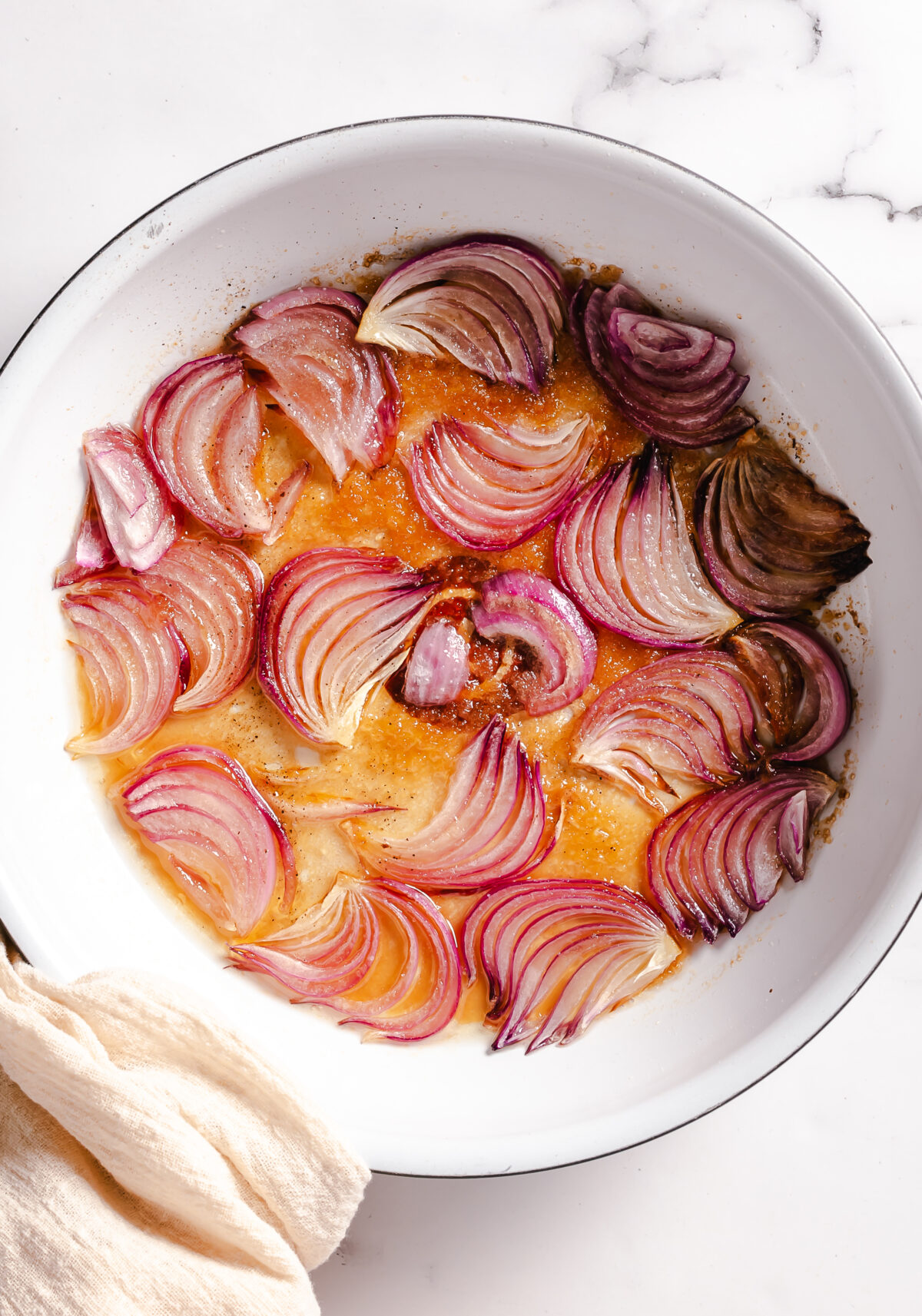 Red onion sliced and cooking in a large white skillet.