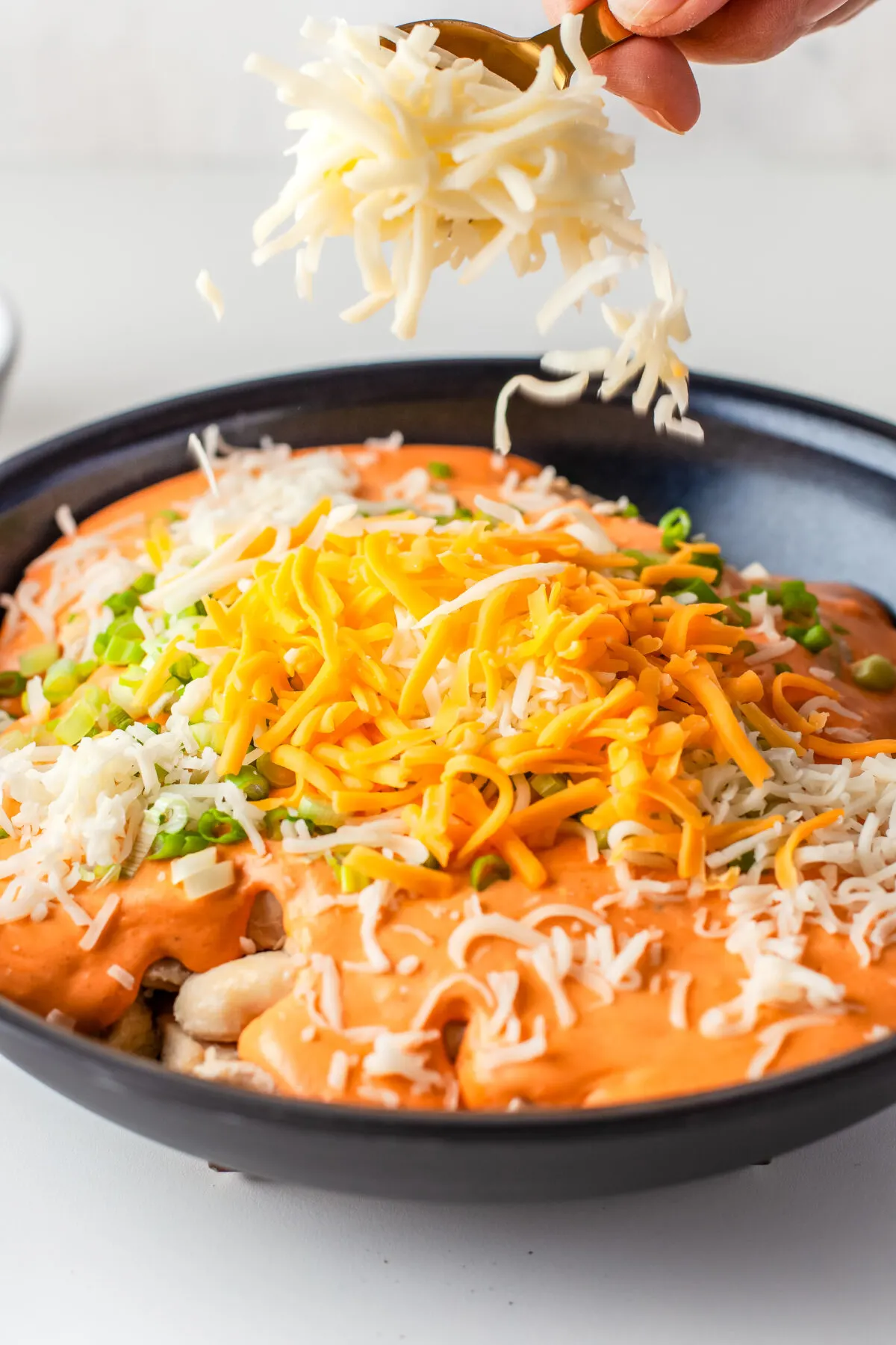 Cheese, chicken and buffalo sauce being combined in a large skillet.