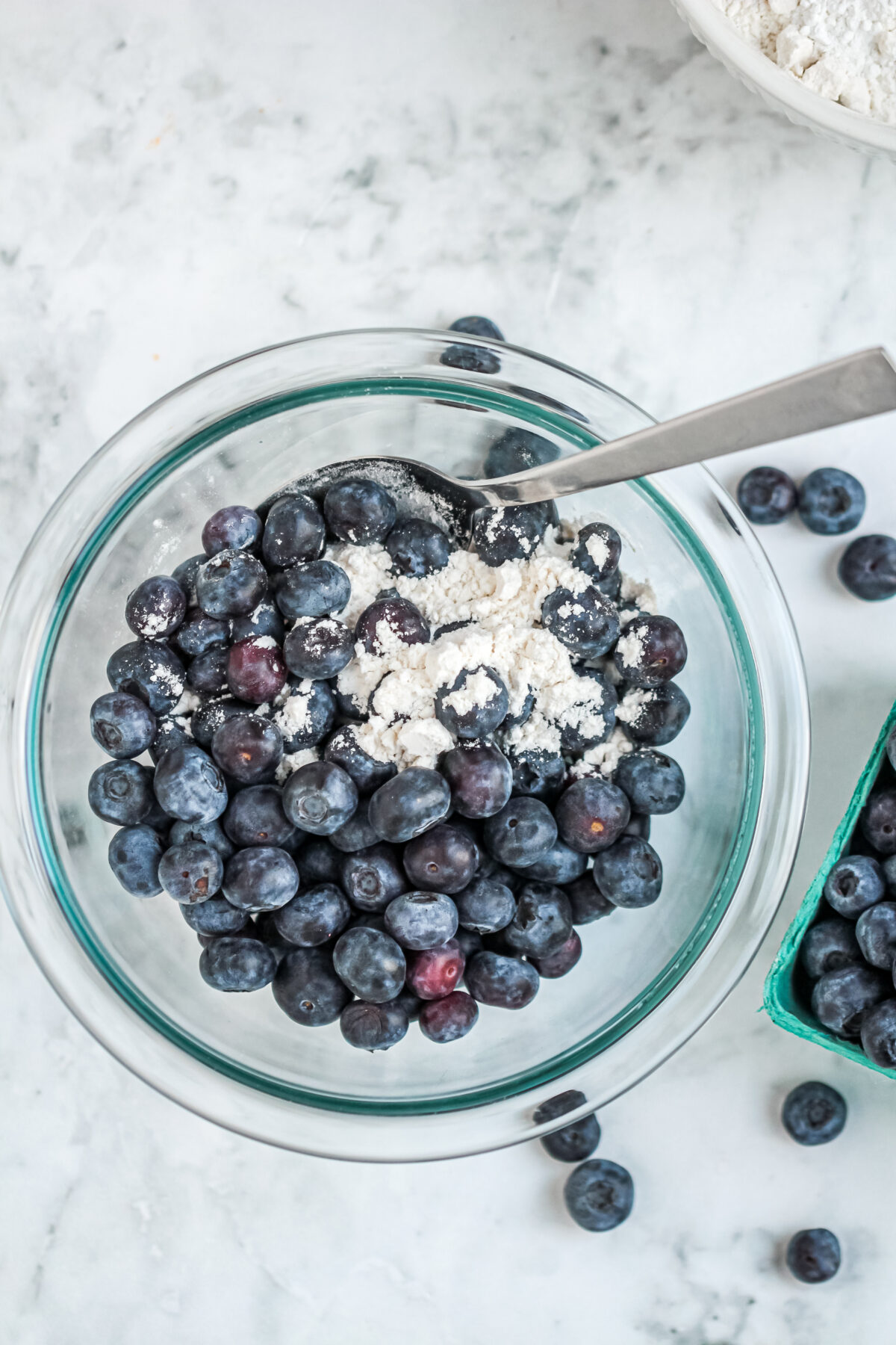 tossing blueberries with flour in a glass bowl.