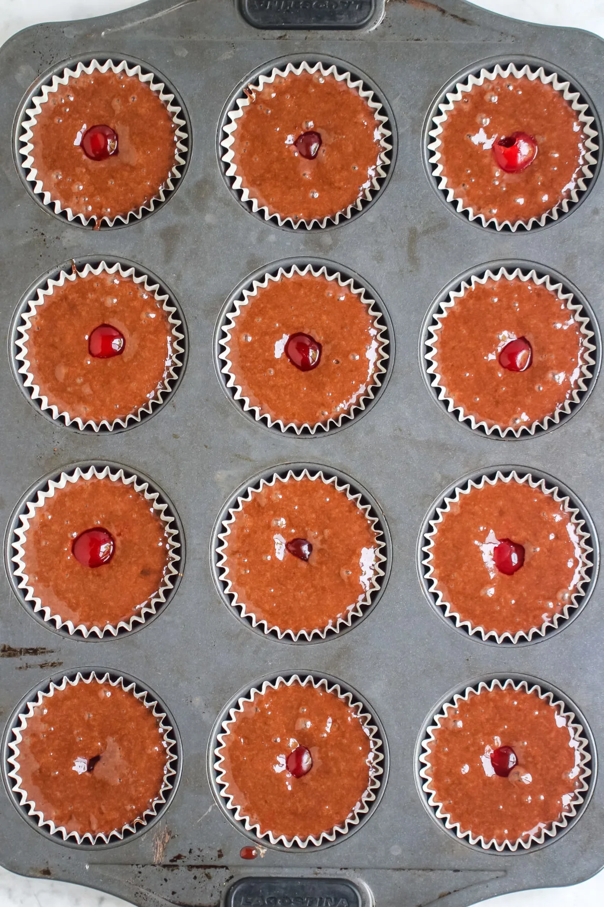 Batter filled cupcake liners with cherries in the middle.