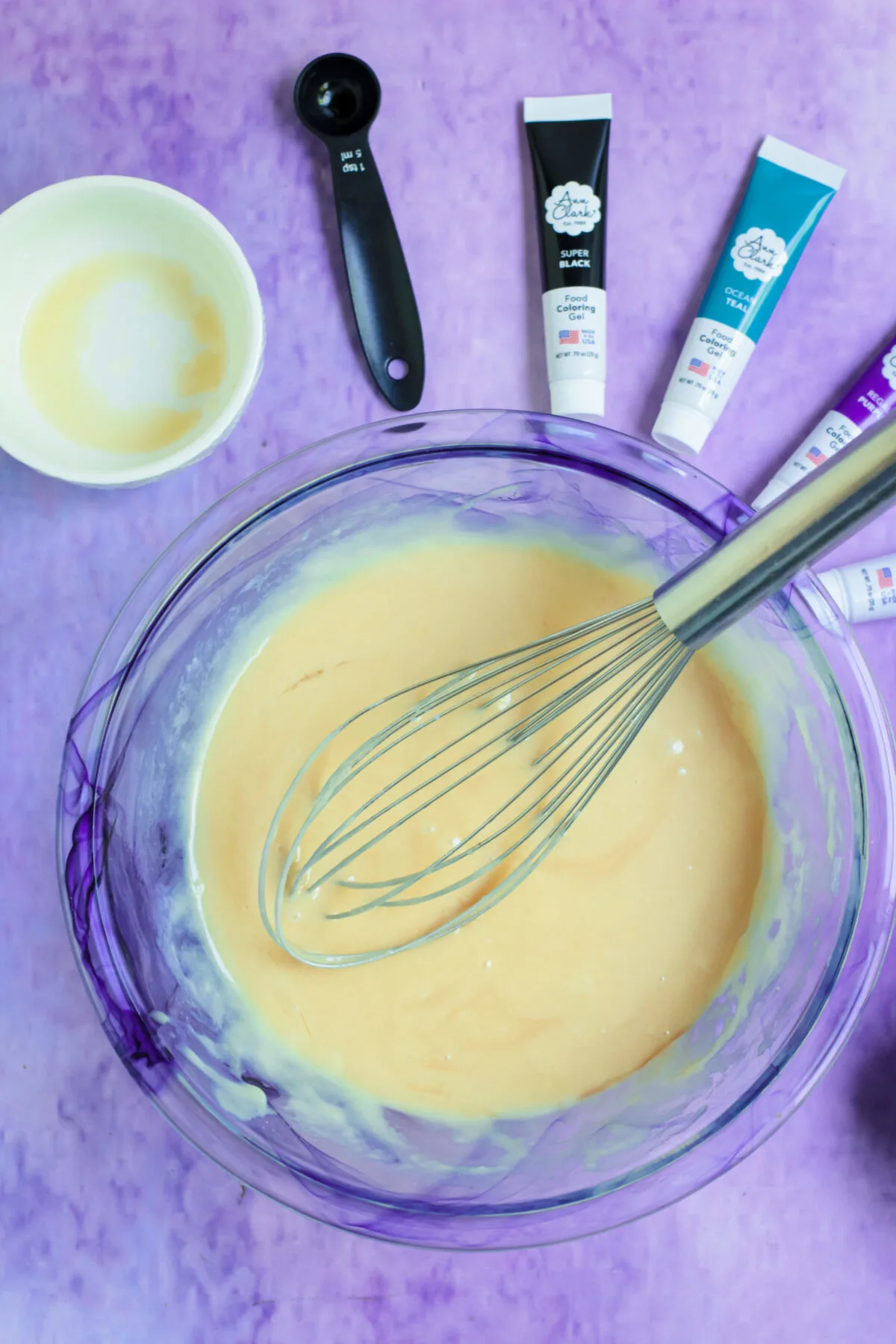 Mixing together vanilla cupcake batter in a large glass bowl with a whisk.