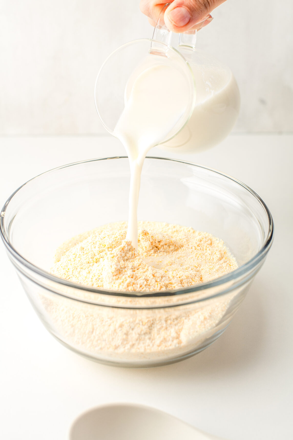 Milk being poured into a glass bowl with cornmeal in it.