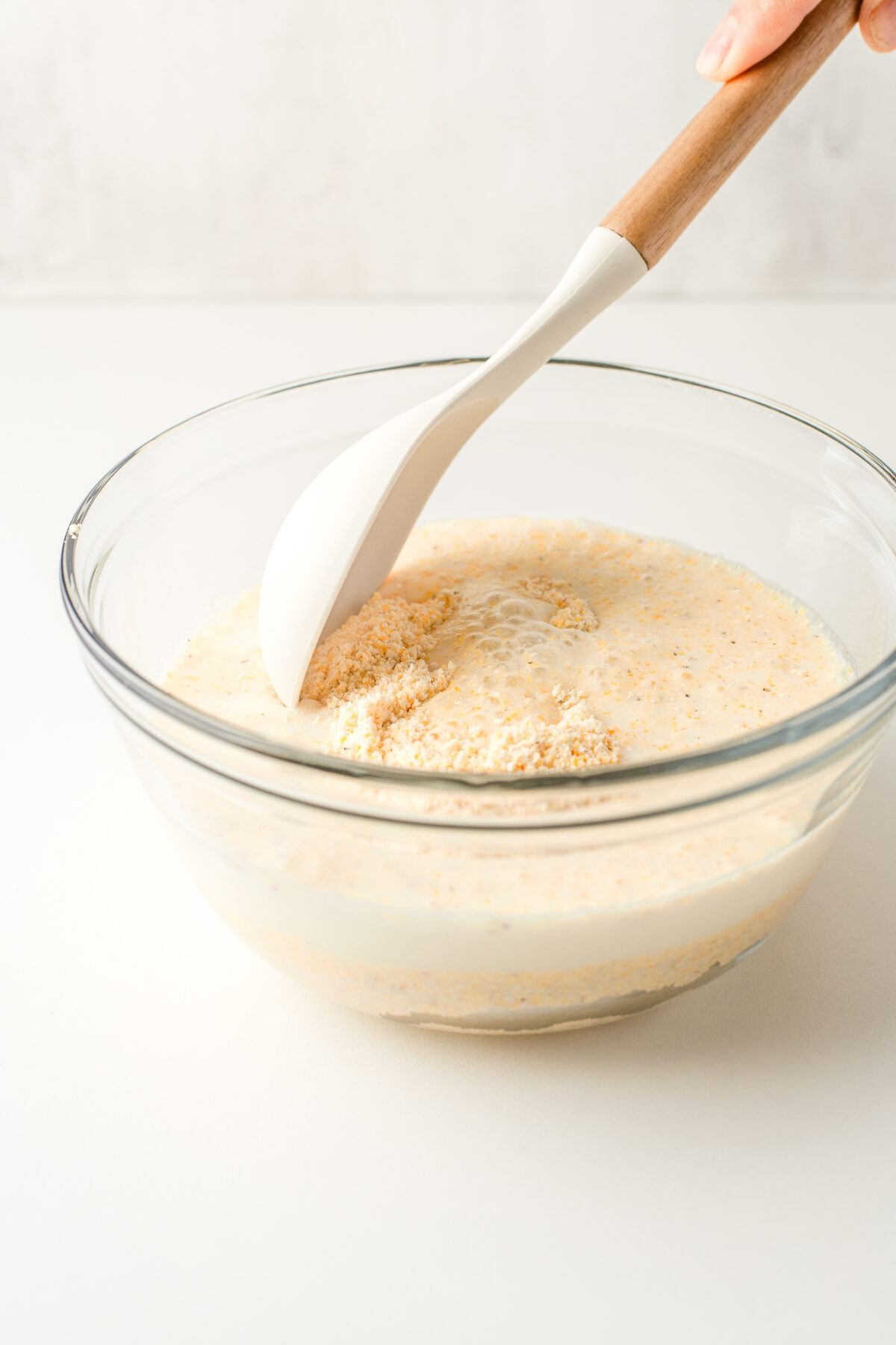 Cornmeal and milk being stirred together in a glass bowl.