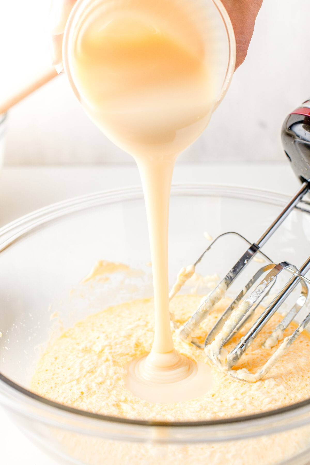 Pouring condensed milk into the wet mixture.