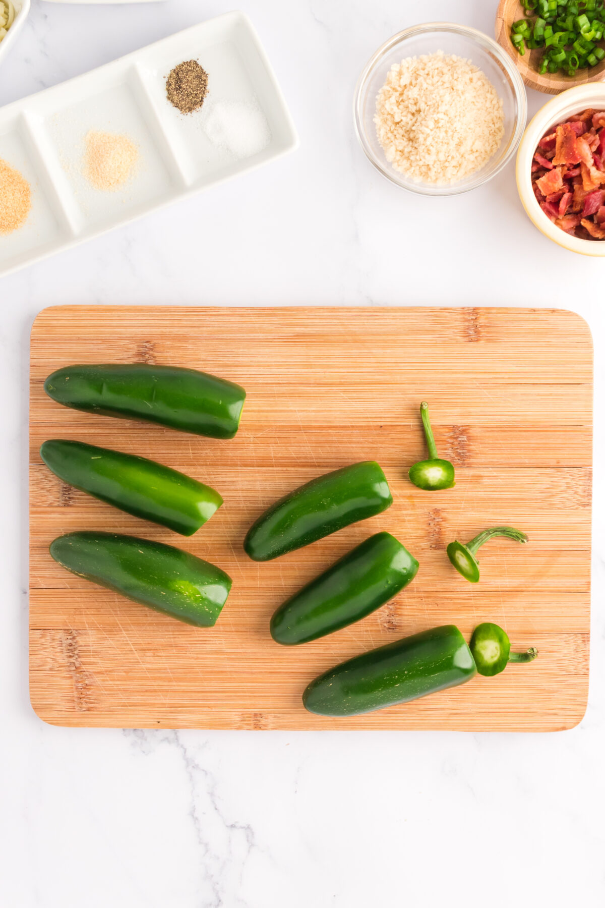 Jalapeno peppers on a cutting board with the tops cut off.