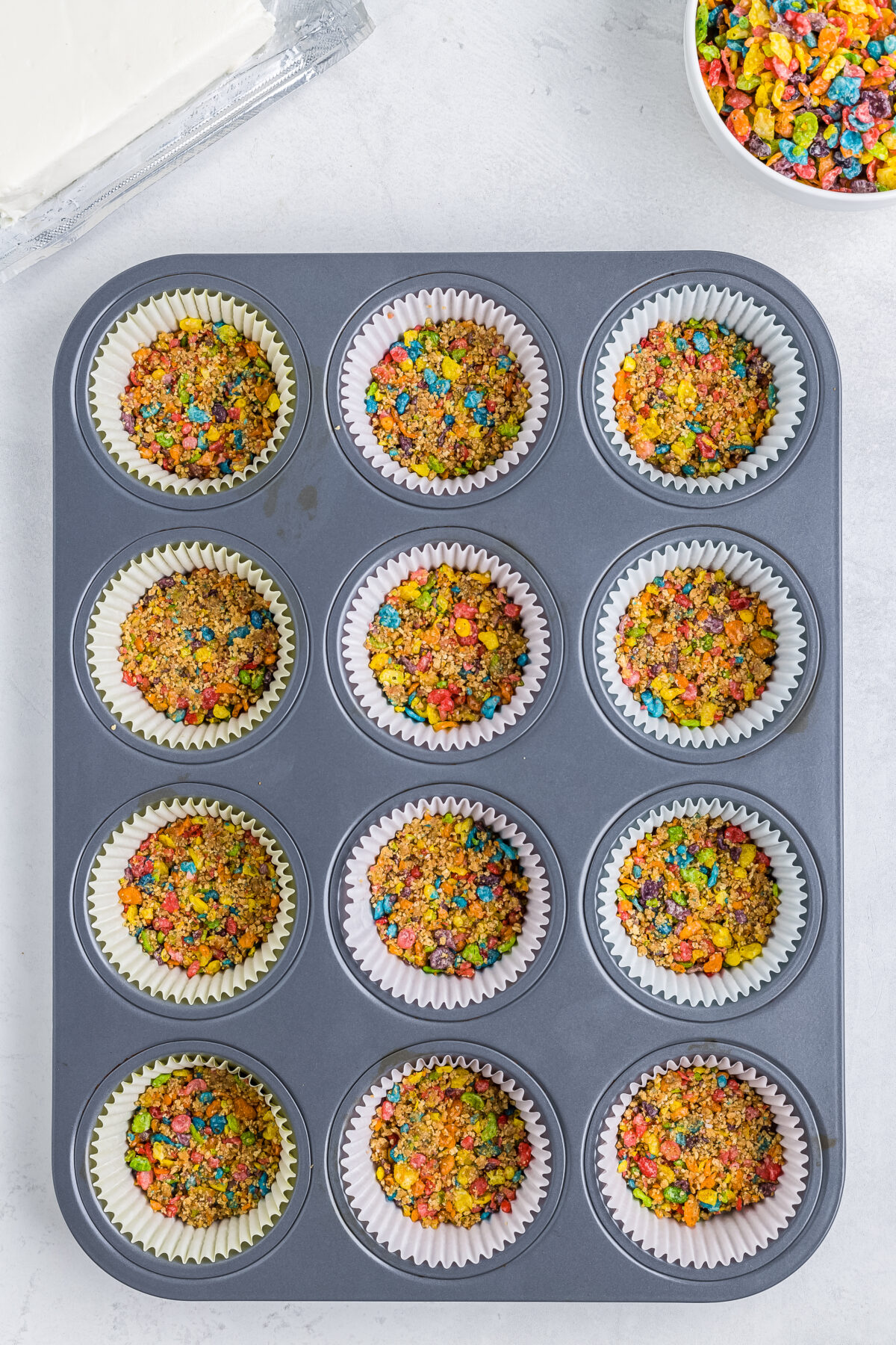 Fruity pebbles crusts in the bottom of cupcake liners in a muffin tin.