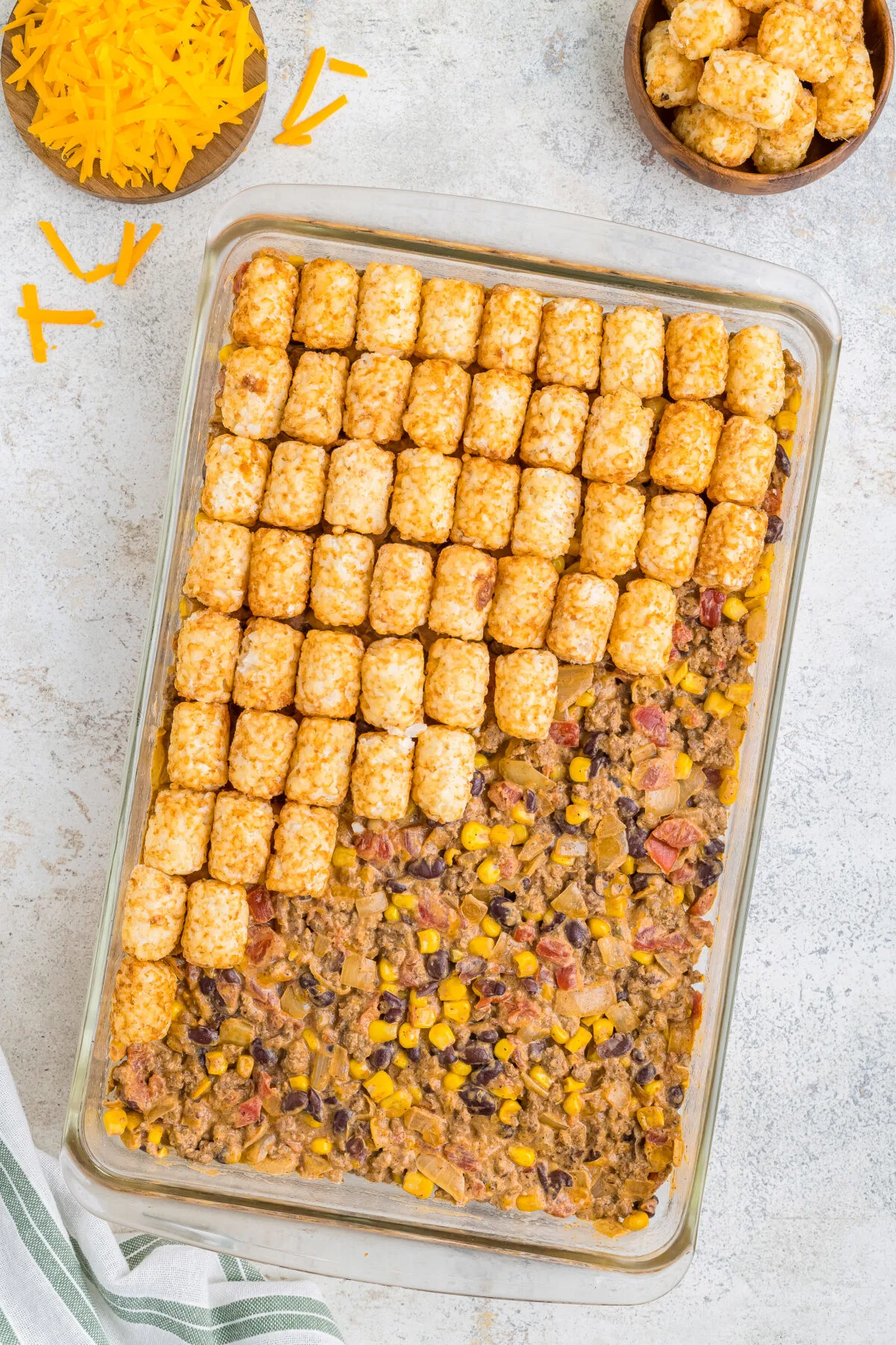 Tater tots being placed onto the casserole.