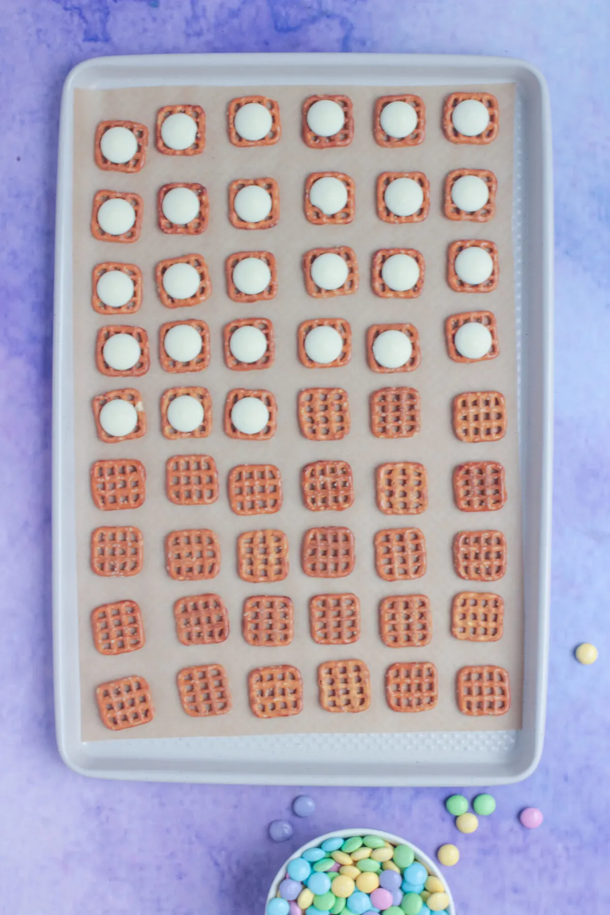 Pretzels layed out on a parchment sheet lined sheet pan with half of them covered with white candy melts.
