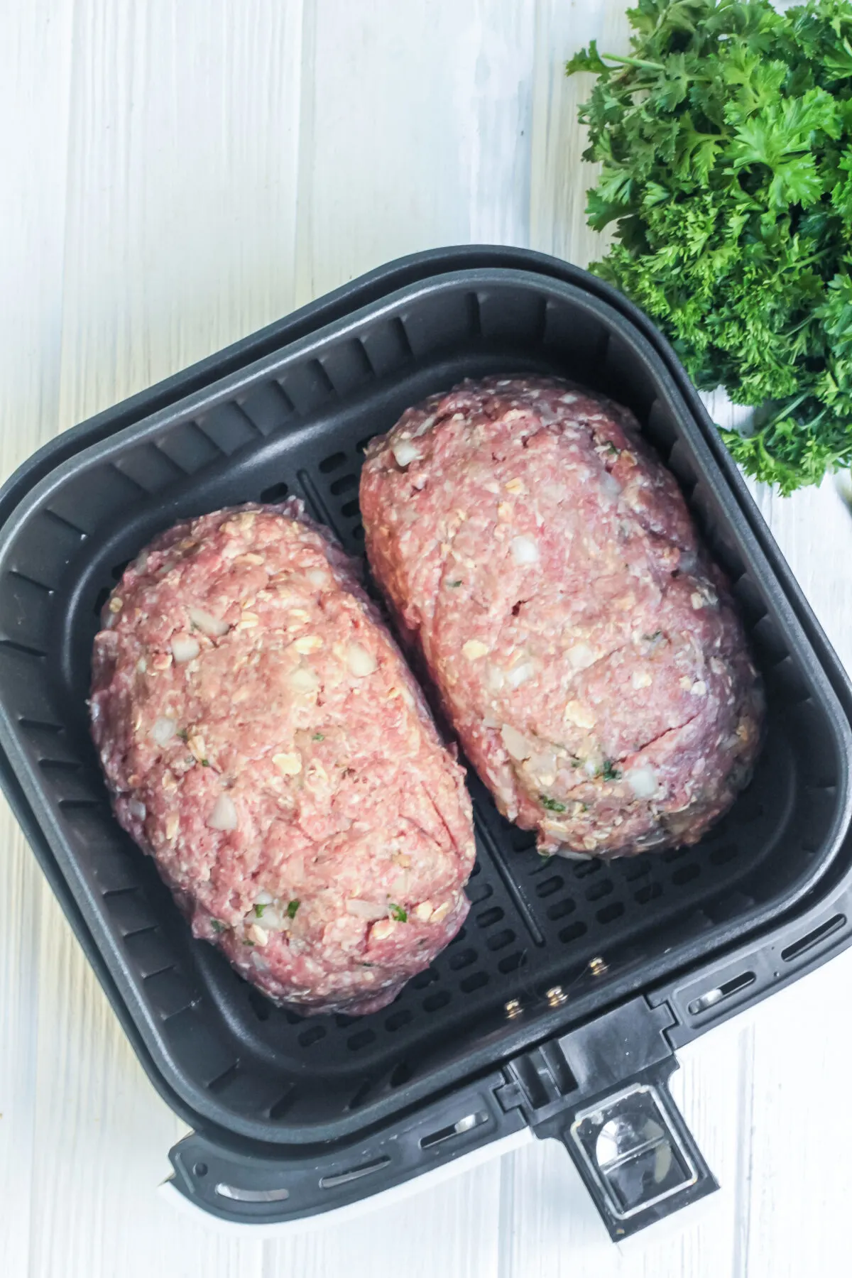 Two meatloaves in an air fryer basket ready to cook.