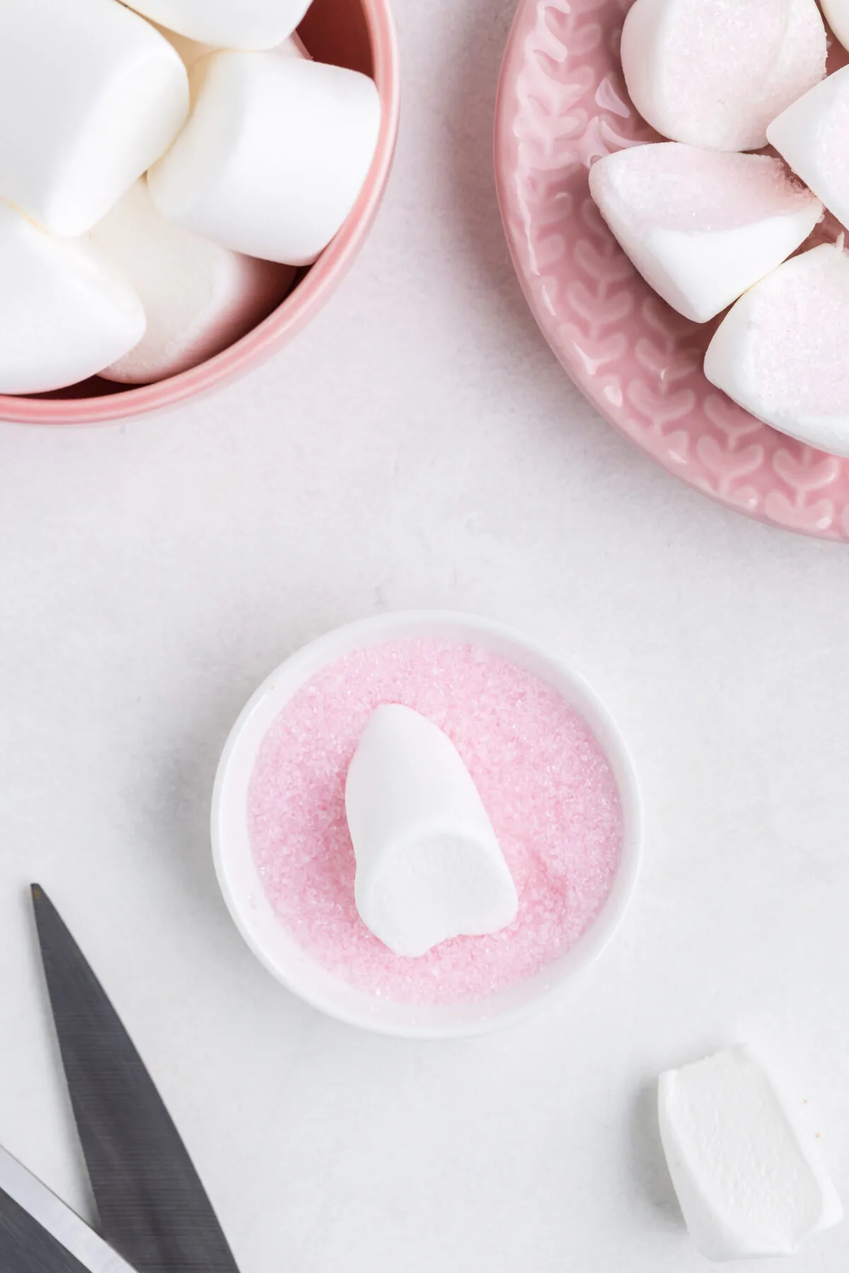 Half a marshmallow sitting in a small bowl of pink sprinkles.