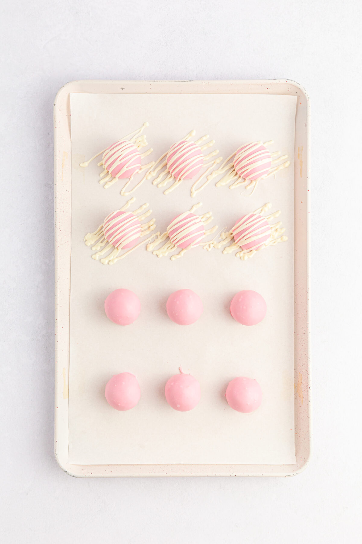 Candy coated dough balls on a sheet pan, half drizzled over with white chocolate.