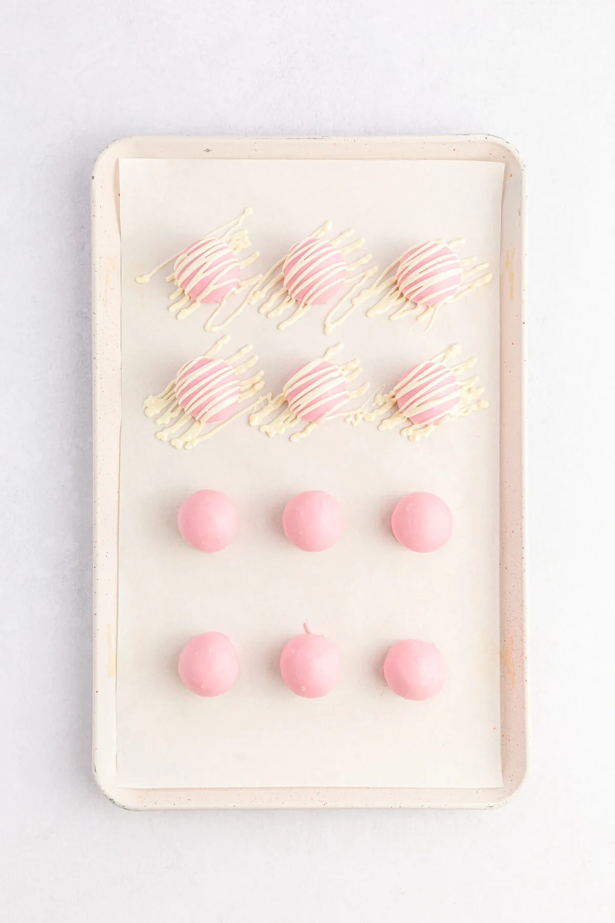 Candy coated dough balls on a sheet pan, half drizzled over with white chocolate.