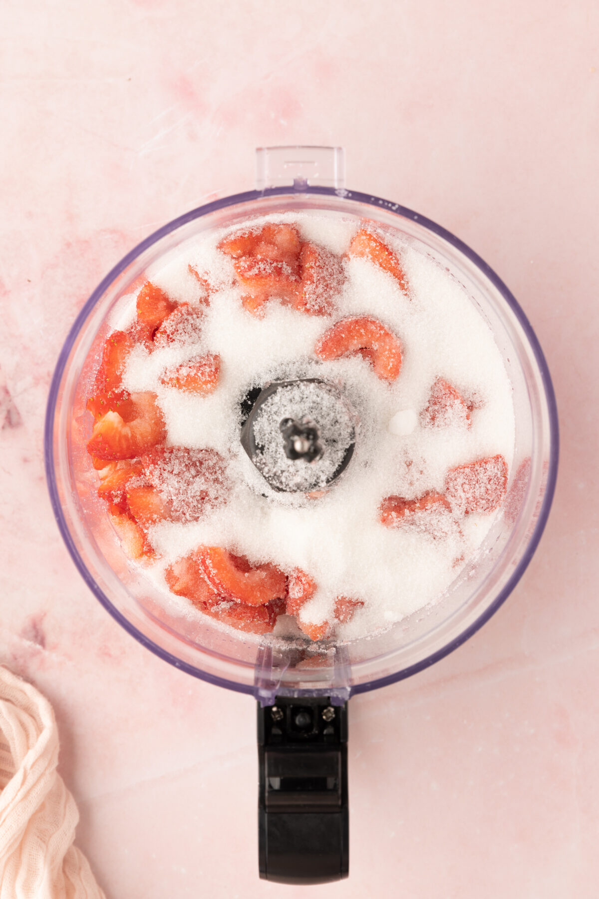 Strawberries and sugar in the bowl of a food processor.